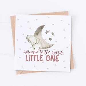 May include: A white card with a pink and gray elephant standing on a crescent moon with stars. The card has a pink polka dot background and the text "welcome to the world LITTLE ONE" in pink.
