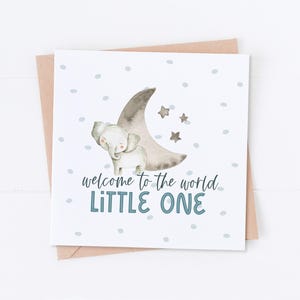 May include: A white card with a gray elephant standing on a crescent moon with stars. The card has blue polka dots and the text "welcome to the world LITTLE ONE".