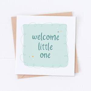 May include: A light blue card with a white border and a light green rectangle in the center. The rectangle has a white, wavy border and the text "welcome little one" in a dark blue cursive font. There are small gold and silver stars scattered around the text.