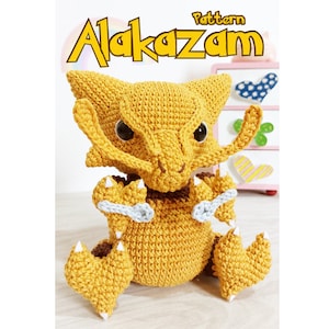 Pode incluir: Um padrão de crochê para Alakazam, um personagem de Pokémon. O padrão é para um Alakazam de crochê amarelo com detalhes brancos. O padrão é mostrado em um fundo rosa e branco.