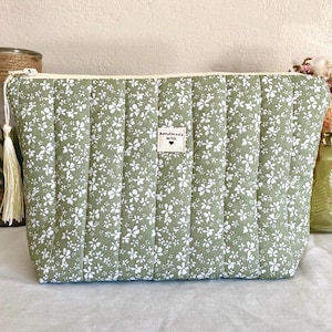Può includere: Un beauty case trapuntato verde salvia con un motivo floreale e una cerniera color crema. La borsa presenta una piccola etichetta con la scritta "handmade with" e un tirazip con nappa. La borsa misura circa 25 cm di larghezza e 18 cm di altezza.