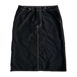 Peut inclure: Une jupe noire avec des détails de couture blanche autour des bords. La jupe a une coupe droite et une longueur mi-longue.
