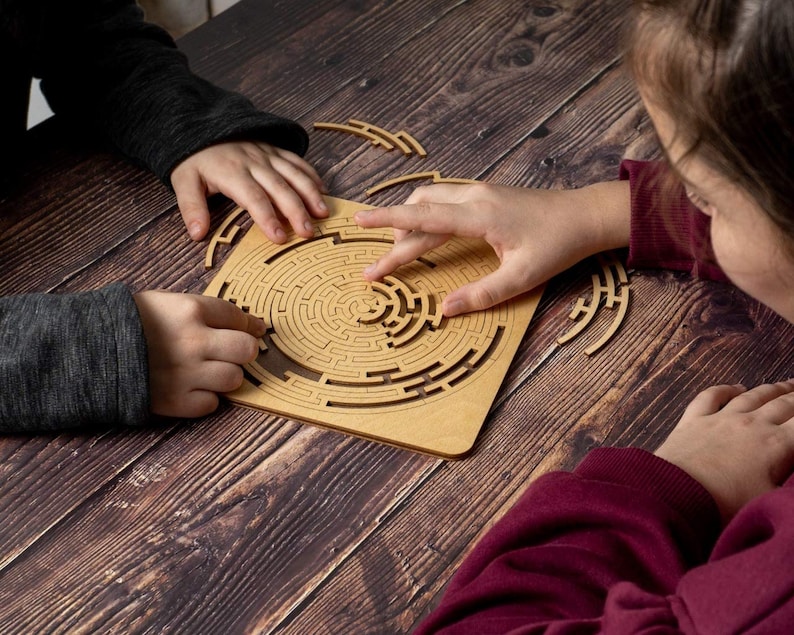 May include: Two people working together to solve a wooden maze puzzle. The puzzle is made of brown wood and has a circular design. The maze is intricate and challenging.
