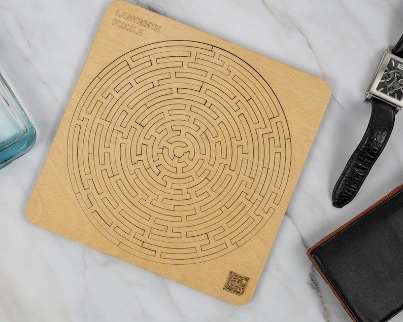 May include: A wooden labyrinth puzzle with a circular design. The puzzle is made of light brown wood and has a natural finish. The text "Labyrinth Puzzle" is printed on the top of the puzzle.
