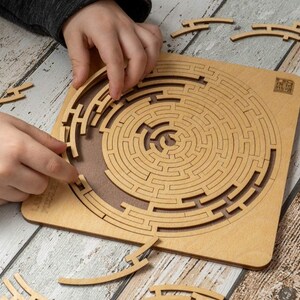 May include: A wooden circular maze puzzle with a brown background. The puzzle is made up of interlocking pieces that form a complex maze. The puzzle is partially assembled, with some pieces missing. The puzzle is on a wooden table.