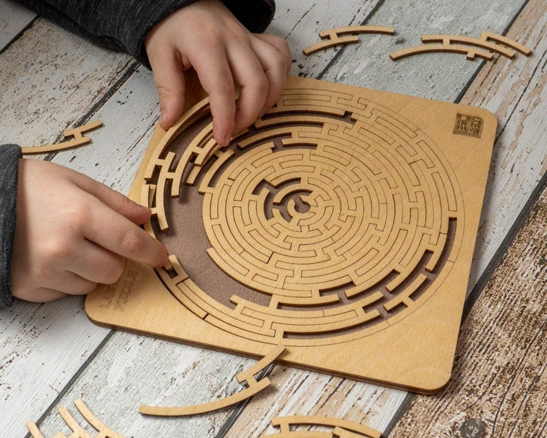 May include: A wooden circular maze puzzle with a brown background. The puzzle is made up of interlocking pieces that form a complex maze. The puzzle is partially assembled, with some pieces missing. The puzzle is on a wooden table.