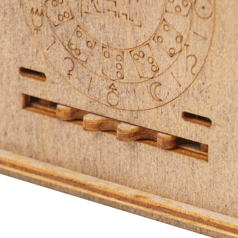 May include: Close-up of a wooden box with a circular design and a gear mechanism. The design features symbols and numbers, possibly representing a calendar or a clock.