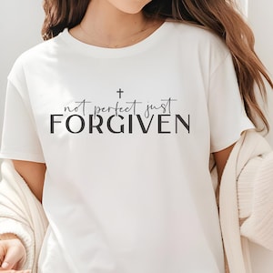 Könnte beinhalten: Weißes T-Shirt mit einem schwarzen Kreuz und dem Text "not perfect just FORGIVEN".