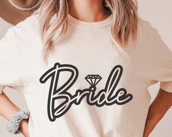 May include: White t-shirt with the word "Bride" in black script with a diamond ring graphic.