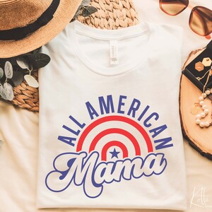 May include: White t-shirt with a blue and red graphic that says "All American Mama" with a star in the center of the graphic.
