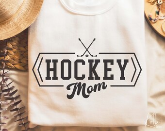 May include: White sweatshirt with a black graphic design that says "Hockey Mom" with two crossed hockey sticks and a puck.