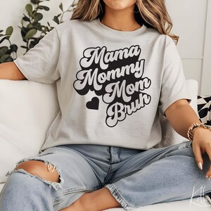 May include: A gray t-shirt with a retro-style graphic that says "Mama Mommy Mom Bruh" in black text.