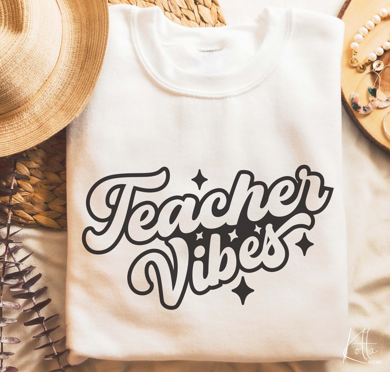 Puede incluir: Sudadera blanca con texto negro que dice "Teacher Vibes" en una fuente retro. El texto est&aacute; rodeado de peque&ntilde;as estrellas.