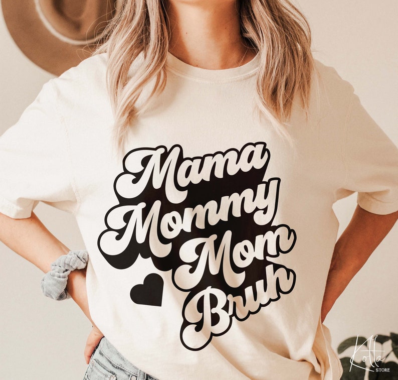May include: White t-shirt with black text that reads "Mama Mommy Mom  Bruh" in a retro font. A small black heart is below the text.