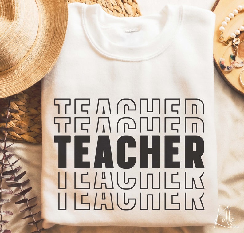 Puede incluir: Sudadera blanca con la palabra "TEACHER" repetida en un dise&ntilde;o retro apilado. La palabra est&aacute; en negro con un contorno blanco.