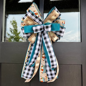 May include: A large teal, black and white checkered bow with a burlap ribbon and a ribbon with a pumpkin and wagon print. The bow is tied to a door.