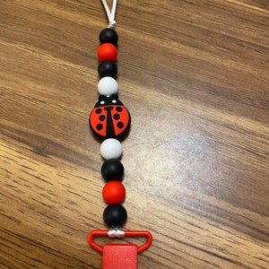 May include: A red, black, and white silicone baby teether with a ladybug charm and a red plastic clip.