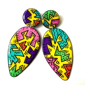 May include: A pair of colorful dangle earrings with a geometric pattern. The earrings are yellow, pink, green, purple, and orange. The earrings are made of resin and have a teardrop shape.