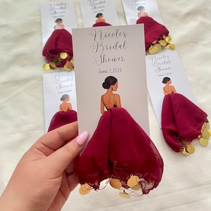Puede incluir: Tarjetas para una despedida de soltera con tela burdeos y detalles de monedas doradas. Las tarjetas muestran una mujer con un vestido burdeos y el texto "Nicole's Bridal Shower, June 7, 2025."