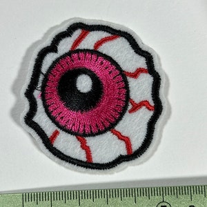 Peut inclure: Un patch pour l'œil brodé en blanc, rouge et noir avec un globe oculaire rose. Le patch mesure environ 5 cm de diamètre.