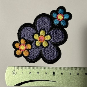 Peut inclure: Patch brodé de fleurs de couleur violette, bleue et orange avec un centre jaune. Le patch mesure environ 5 pouces de large.