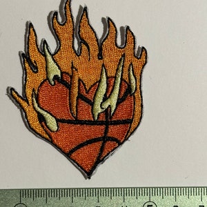 Puede incluir: Parche bordado para planchar con forma de corazón con un balón de baloncesto en el centro y llamas alrededor. El balón de baloncesto es naranja y marrón con costuras negras. Las llamas son naranja y amarillas.
