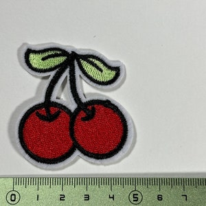 Op de afbeelding: Rode geborduurde kers-patch met groene bladeren. De patch is ongeveer 5 cm breed en 4 cm hoog.