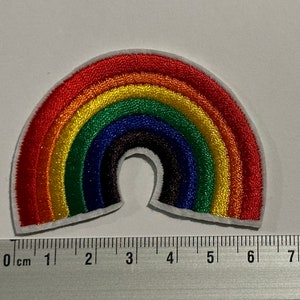 Può includere: Un cerotto ricamato a forma di arcobaleno con un contorno bianco. Il cerotto è largo circa 6 cm e presenta i colori rosso, arancione, giallo, verde, blu, indaco e viola.