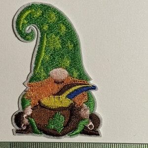 Peut inclure: Patch brodée thermocollante représentant un gnome vert portant un chapeau vert avec un oiseau jaune et bleu dans sa main.