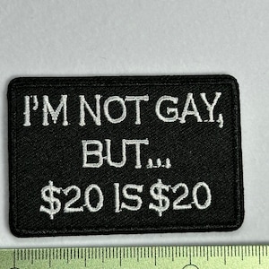 Może przedstawiać: Czarna haftowana naszywka z białym tekstem, który brzmi "I'M NOT GAY, BUT... 20€ IS 20€".