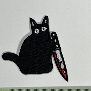 Puede incluir: Parche de hierro negro bordado de un gato negro sosteniendo un cuchillo rojo y blanco.