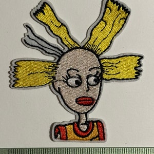 May include: Embroidered iron-on patch featuring a cartoon character with yellow hair, a red and yellow shirt, and a white background.