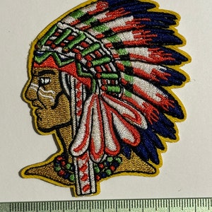Op de afbeelding: Gestikt patch van een inheemse Amerikaan met een kleurrijke hoofdtooi met rode, witte, blauwe en groene veren. Het patch is omrand met gouden draad en is ongeveer 5 inch breed.