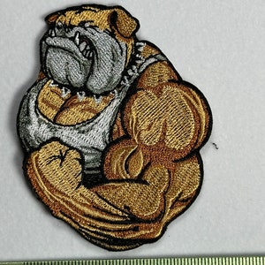 Peut inclure: Patch brodé représentant un bouledogue brun et blanc portant un débardeur blanc et fléchissant ses muscles biceps. Le bouledogue regarde vers la gauche.