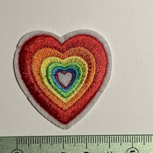 Op de afbeelding: Regenboogvormige geborduurde patch in de vorm van een hart met een witte rand. De patch is ongeveer 5 cm breed.