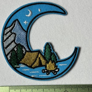 Peut inclure: Un patch brodé en forme de croissant de lune bleu avec une scène de montagne, une tente, un feu de camp et un pin. La lune a un croissant de lune blanc et une étoile blanche à l'intérieur.