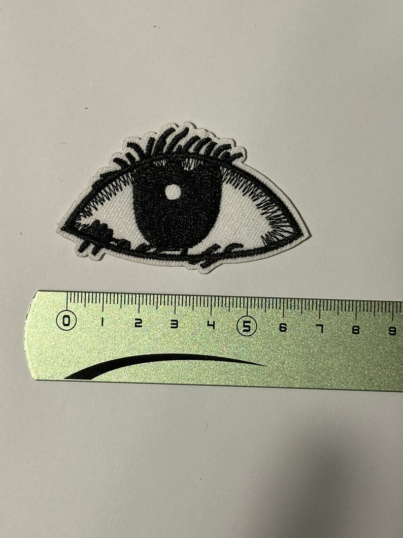 May include: White embroidered eye patch with black stitching and a black eye. The patch is approximately 5 cm wide.