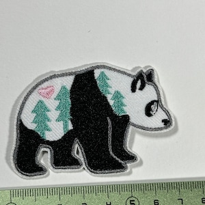 Peut inclure: Un écusson thermocollant brodé représentant un panda blanc et noir avec une scène de forêt sur son dos. Le panda marche vers la droite. La scène de forêt comprend des arbres verts et un coucher de soleil rose.