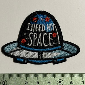 May include: Embroidered iron-on patch featuring a blue and white UFO with the text "I need my space" in white with red stars.