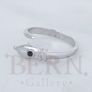 Könnte beinhalten: Ein silberner Schlangenring mit einem schwarzen Edelsteinauge. Der Ring ist offen und verstellbar.