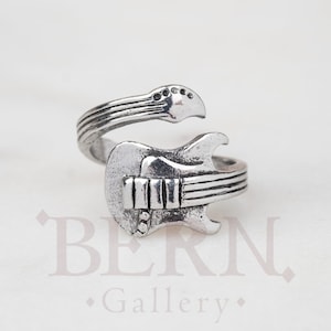 May include: A silver-toned adjustable ring shaped like an electric guitar. The ring features a detailed design of the guitar's body, neck, and strings.