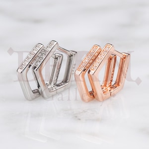 Peut inclure: Deux paires de boucles d'oreilles créoles, l'une en argent et l'autre en or rose, avec un design hexagonal double et des pierres de zircone cubique transparentes.