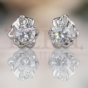 May include: A pair of silver earrings with a clear crystal stone in the center of each earring. The earrings have a delicate floral design.