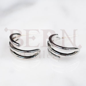 May include: A pair of silver hoop earrings with a triple band design.