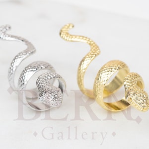 Puede incluir: Dos anillos en forma de serpiente, uno plateado y otro dorado. Los anillos están enrollados y tienen una superficie texturizada.