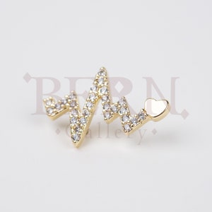 May include: Gold-tone heart beat charm with clear cubic zirconia stones and a small heart charm at the end.