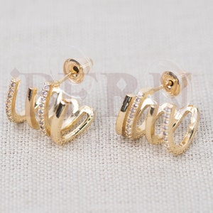 Puede incluir: Un par de pendientes de aro de oro con un diseño de aro triple. Cada aro está acentuado con una fila de piedras de circonita cúbica transparentes.