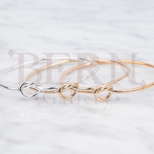 May include: Three gold and silver bangle bracelets with a knot design. The bracelets are stacked on top of each other.