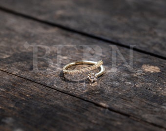May include: A gold ring with a single, clear stone set in the centre. The ring is adorned with small, clear stones along the band.