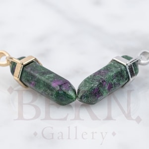 May include: Two green and purple gemstone pendants with gold and silver settings. The pendants are shaped like long, thin points.